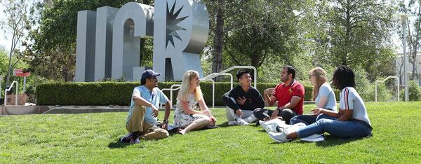 students sitting on the lawn near UCR sign